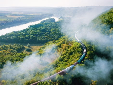 Moving train on railway with high column of smoke, flowing river, hills and railway on the foreground, fields on the other shore in Moldova